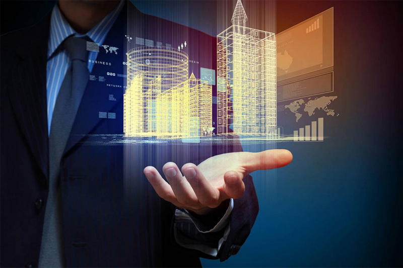 A person in a suit holds a holographic representation of buildings and data charts.